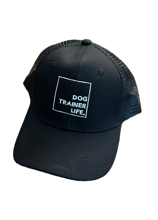 Black cap with 'Dog Trainer Life' text on a wooden table